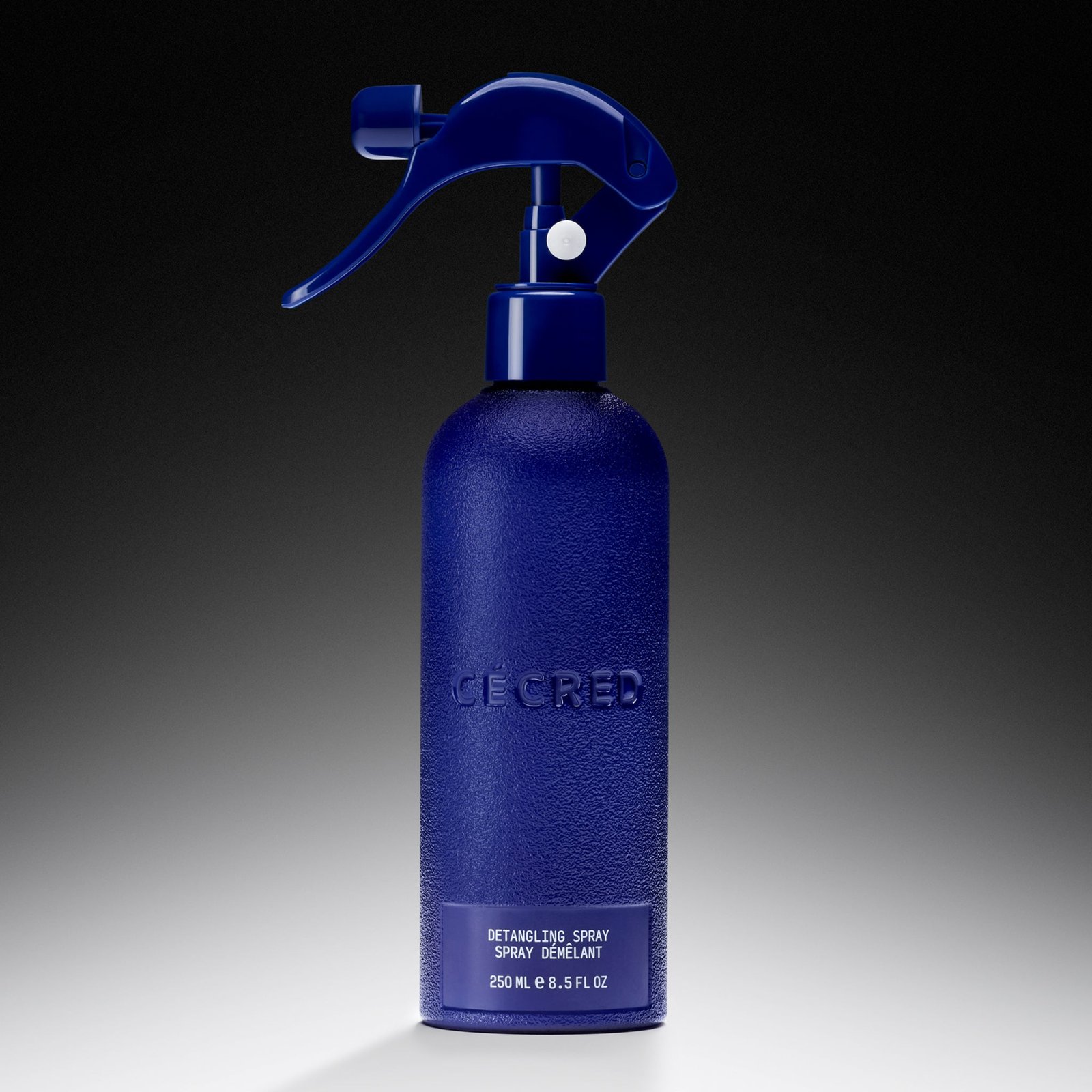 Cécred Detangling Spray in a blue spray bottle on a gradient background